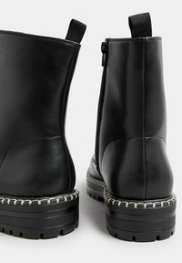 Botas de tobillo de cuero negro con un acabado suave, cierre de cremallera lateral y un acento blanco cosido alrededor de la suela de goma.