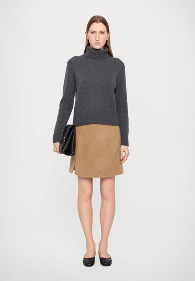 Dark gray wool turtleneck sweater paired with a tan fuzzy mini skirt. Black handbag with smooth finish. Model wearing black flats.