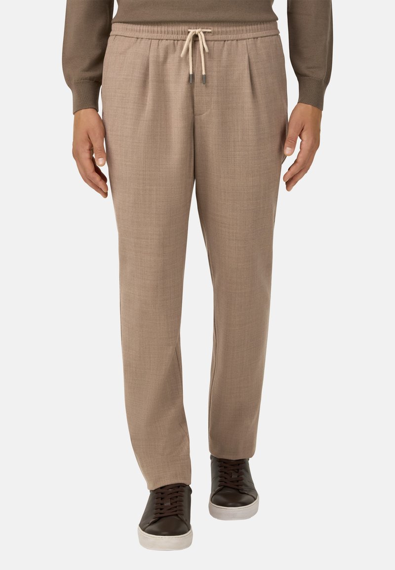 Světlé béžové kalhoty na míru s hladkým povrchem, elastickým pasem a nastavitelnou šňůrkou, kombinované s tmavohnědými teniskami.