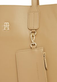 Borsa tote in pelle beige con logo dorato, portacarte staccabile e dettagli di cucitura semplici. Texture liscia con chiusura zip.