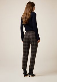 Marineblå ribstrikket sweater, ternede højttaljede bukser i brune og grå nuancer, koniske ben, sorte ankelstøvler med hæl. Struktureret strikstof.