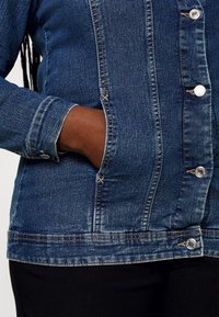 Jeansjacka i mörkblått med silverknappar, detaljerad sömnad och en sidoficka. Har en strukturerad passform och en lätt urvattnad textur.