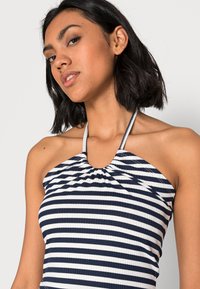 Top halter listrado em azul-marinho e branco, feito em tecido canelado, com decote franzido e alças finas.
