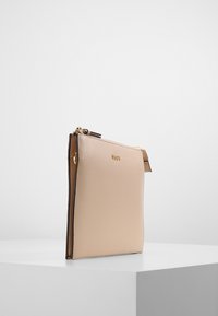 Beige synthetic leather pouch with a gold zipper, slim design, smooth texture, and a small accent tab on the side.