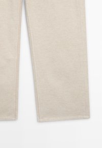 Beige ribbed corduroy pants with a straight fit and visible seams. The texture is soft with a subtle sheen, lacking additional embellishments.
