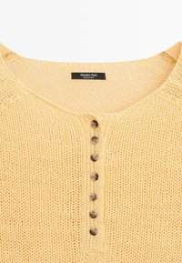 Lysegul strikket bluse med syv brune knapper og en kravelabel med teksten "Massimo Dutti, Made in China."