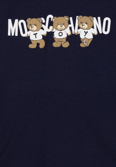 Sötétkék póló, amelyen három rajzfilmszerű medve látható fehér ingben, felettük a "Moschino Toy" felirat dőlt, stílusos betűtípussal.