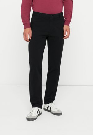Black cotton pants with a straight leg design, featuring standard pockets and a button closure. Worn with white and gray sneakers.