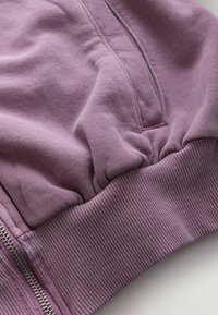 Lila bomullssweatshirt med en strukturerad ribbad nederkant och ärmar, med en slät dragkedja längs sidan och en mjuk, avslappnad passform.
