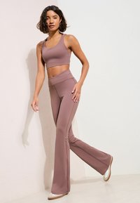 Set sportiv elastic în culoarea mov, format dintr-un top scurt mulat și colanți evazați. Materialul are o textură netedă și un design cu talie înaltă.
