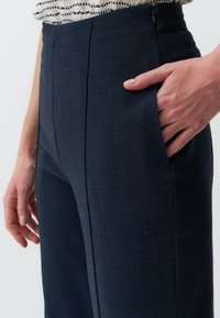 Ciemnoniebieskie spodnie o fakturowanej tkaninie, z boczną kieszenią i subtelnym detalem marszczenia z przodu, dobrze dopasowane w talii.