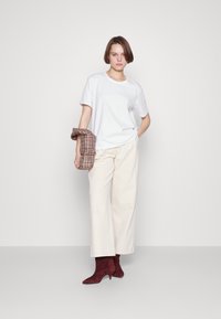 White short-sleeve t-shirt, cream wide-leg pants, and burgundy suede ankle boots. Plaid patterned bag held over one arm. Simple and modern design.