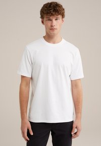 Vit bomullströja med rund halsringning och korta ärmar, med en slät textur och rak passform. Bärs med svarta byxor.