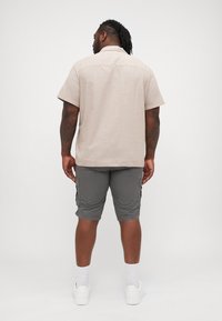 Camicia a maniche corte color beige chiaro con una consistenza morbida, abbinata a pantaloni cargo grigi con tasche laterali e una vestibilità rilassata. Sneakers bianche completano il look.