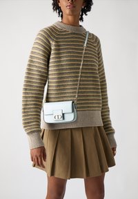 Suéter a rayas en beige y oliva, falda marrón plisada y un bolso cruzado azul claro con cierre y correa de cadena. Textura suave.