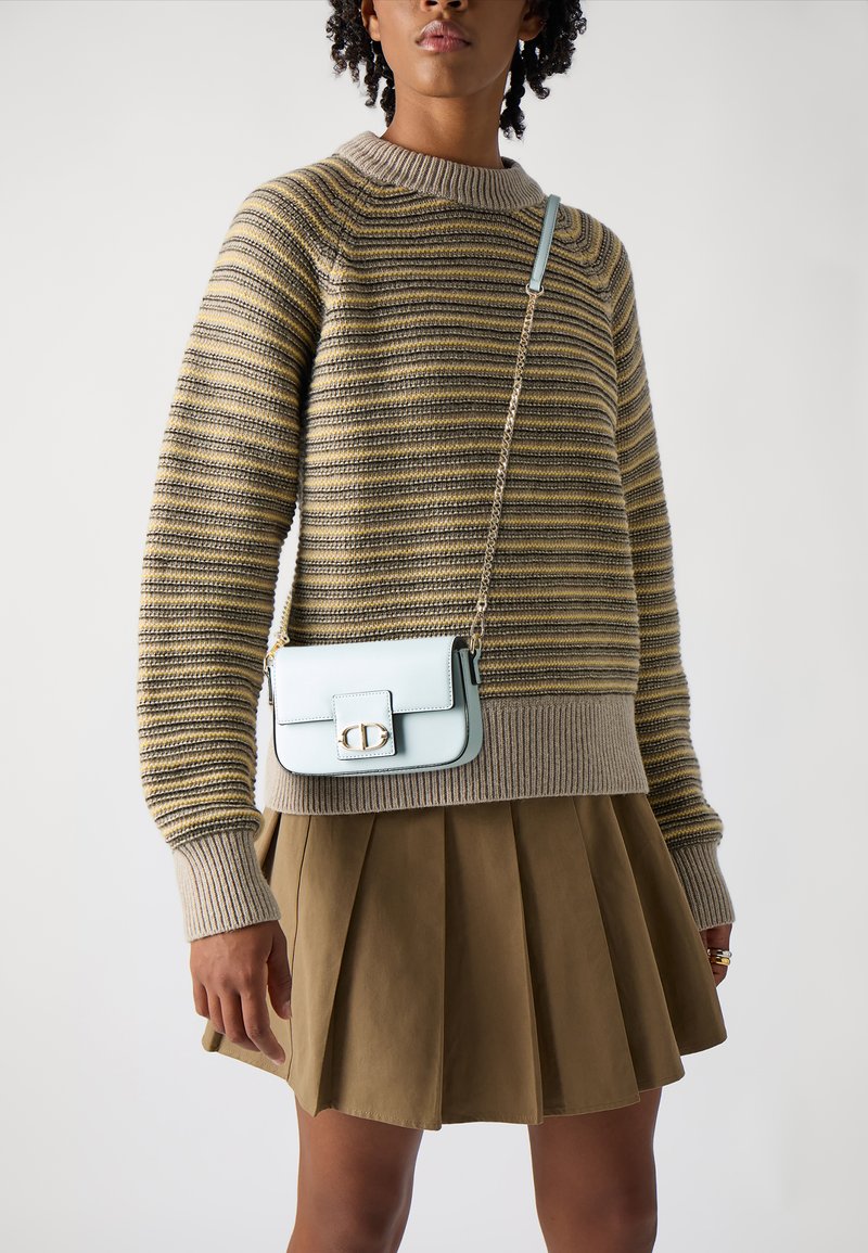 Suéter a rayas en beige y oliva, falda marrón plisada y un bolso cruzado azul claro con cierre y correa de cadena. Textura suave.