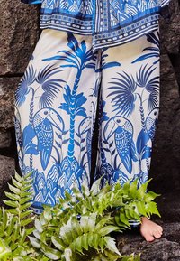 Blue and cream wide-leg pants with a tropical bird and foliage pattern. Lightweight fabric, smooth texture, detailed accents at the hem.