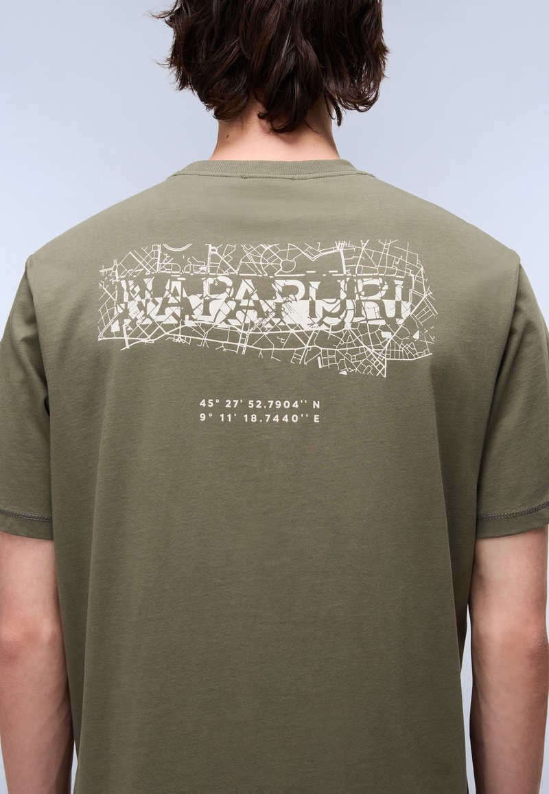 Oliwkowy bawełniany T-shirt z białym nadrukiem graficznym przedstawiającym linie mapy i współrzędne na plecach. Krótkie rękawy, standardowy krój.