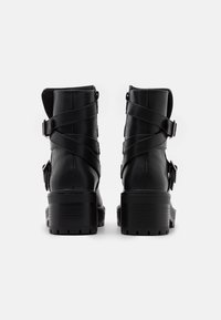 Botines negros de cuero con correas en cruz y hebillas, una suela gruesa texturizada y un alto tacón cuadrado.