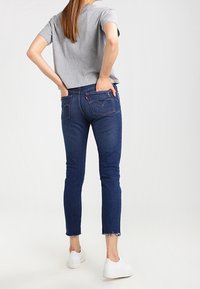 Donkere denim jeans met rafelige zoom en twee achterzakken, gedragen met een grijs T-shirt met korte mouwen en witte sneakers.