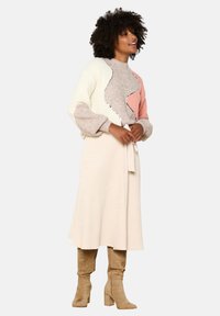 Multicolored knitted sweater with gray, beige, pink, and cream sections, paired with a cream midi skirt and beige knee-high boots.