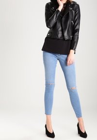 Svart läderbikerjacka över en svart topp, i kombination med ljusblå skinny jeans med knäskador och svarta högklackade skor.