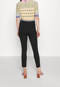 Svarta tajta byxor parat med en kortärmad topp i flerfärgat mönster. Toppens krage är rosa och den har olika geometriska mönster.