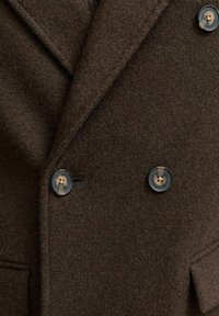 Blazer de lana marrón con un diseño de doble botonadura, solapas de muesca y botones redondos con centros contrastantes. Detalle de tela texturizada visible.