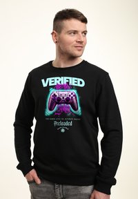 Sudadera negra con un vibrante texto gráfico "VERIFICADO" y un diseño de controlador de videojuegos, con acentos en azul y morado. Confeccionada con tejido suave.