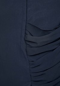 Marineblå topp i mjukt tyg med veckade detaljer på ena sidan, vilket ger en texturerad look. Slätt, lätt material.