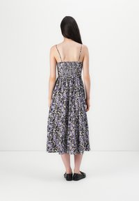 Blumenkleid in Midi-Länge mit verstellbaren Spaghetti-Trägern, gerafftem, gesmocheltem Oberteil in Lila und Schwarz, fließendem Rock und schwarzen Ballerinas.