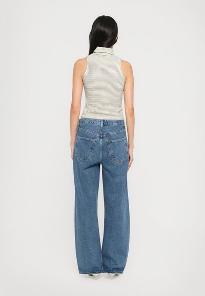 Top senza maniche a righe con colletto alto, abbinato a jeans blu a gamba larga con tasche posteriori e vestibilità rilassata.
