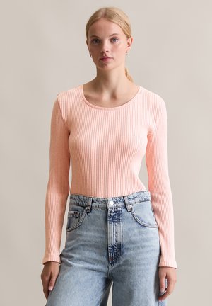 Haut à manches longues côtelé en doux rose pastel, avec un col rond, associé à un jean en denim délavé taille haute.