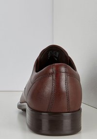 Brune lærskos med poleret finish, lav hæl og synlige syninger bagpå. Enkel, strømlinet design uden udsmykninger.