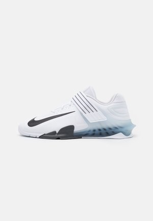 Chaussure de sport blanche avec un swoosh Nike noir, une sangle rayée ajustable, un col en mesh et un support de talon en dégradé bleu sur un fond uni.