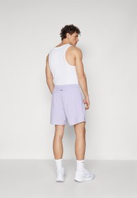 Licht lila sportshorts met een elastische tailleband en zijsplitsingen, gedragen met een wit tanktop, gezien vanuit de achterkant.