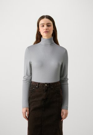 Pull en col montant gris avec de longues manches, en matière texturée, associé à une jupe en denim brun foncé avec poches avant et fermeture à boutons.