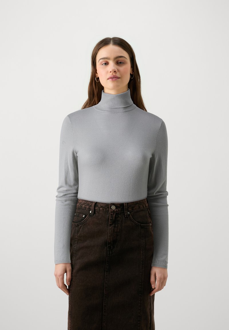 Pull en col montant gris avec de longues manches, en matière texturée, associé à une jupe en denim brun foncé avec poches avant et fermeture à boutons.