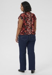 Haut multicolore avec un imprimé léopard rouge, noir et rose, associé à un jean en denim foncé. Le haut a des manches courtes et une coupe décontractée.
