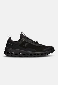 Chaussure de sport noire avec une tige en mesh texturé, semelle épaisse et rembourrée, et découpes de ventilation. Équipée de lacets intégrés et d'une boucle au talon.