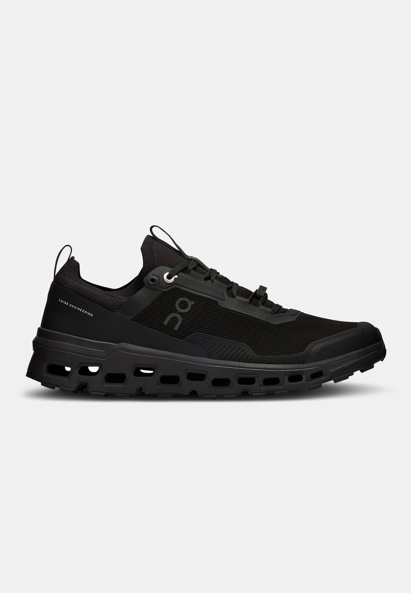 Chaussure de sport noire avec une tige en mesh texturé, semelle épaisse et rembourrée, et découpes de ventilation. Équipée de lacets intégrés et d'une boucle au talon.