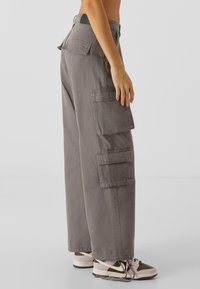 Pantalons cargo en coton gris avec des jambes larges, plusieurs poches latérales et une taille haute. Portés avec des baskets marron et rose.