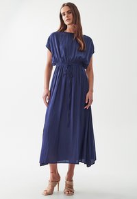 Laivansinis maxi-mekko lyhyillä dolman-hihansuilla, vyötäröltä kiristetty ja virtaava hameosa. Kangas vaikuttaa kevyeltä ja sileältä.