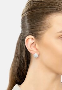 Pendientes de plata en un diseño floral, con superficie texturizada y bordes redondeados. Llevados en la oreja izquierda, vista en primer plano.