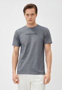 Camiseta gris de manga corta con el texto "LO SIENTO, LLEGO TARDE" en un tono oscuro en el pecho, hecha de una tela suave y texturizada.