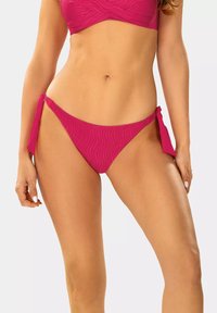 Różowy dół bikini o falistej teksturze, z bocznymi wiązaniami dla regulacji. Skrojony w klasycznym, minimalistycznym kształcie. Gładkie wykończenie materiału.