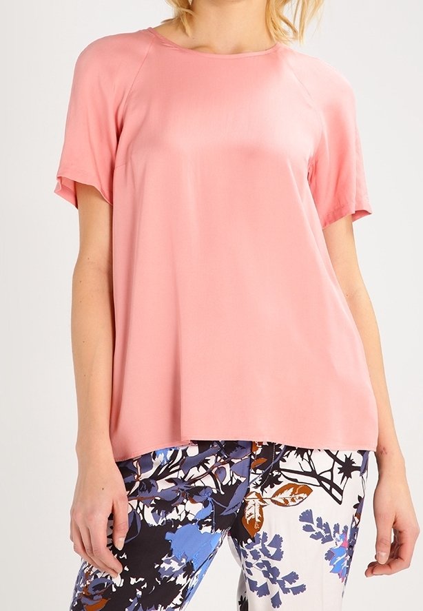 Femme portant un haut rose ample à manches courtes associé à un pantalon blanc orné de motifs floraux bleus, noirs et marron.
