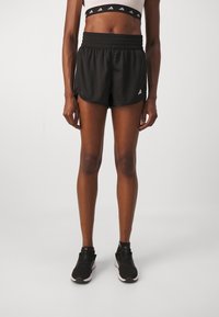 Black athletic shorts with an elastic waistband, side slits, and a small white logo on the left leg. Worn with black running shoes.