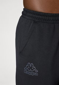 Crne trenirke napravljene od mekog materijala, sa elastičnom trakama u struku, bočnim džepom i Kappa logotipom u tamnoplavoj boji na gornjem bedru.