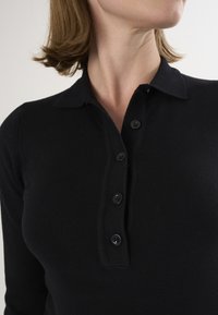 Sort strikket polo med blød tekstur, med krave, fem sorte knapper og en tætsiddende pasform.